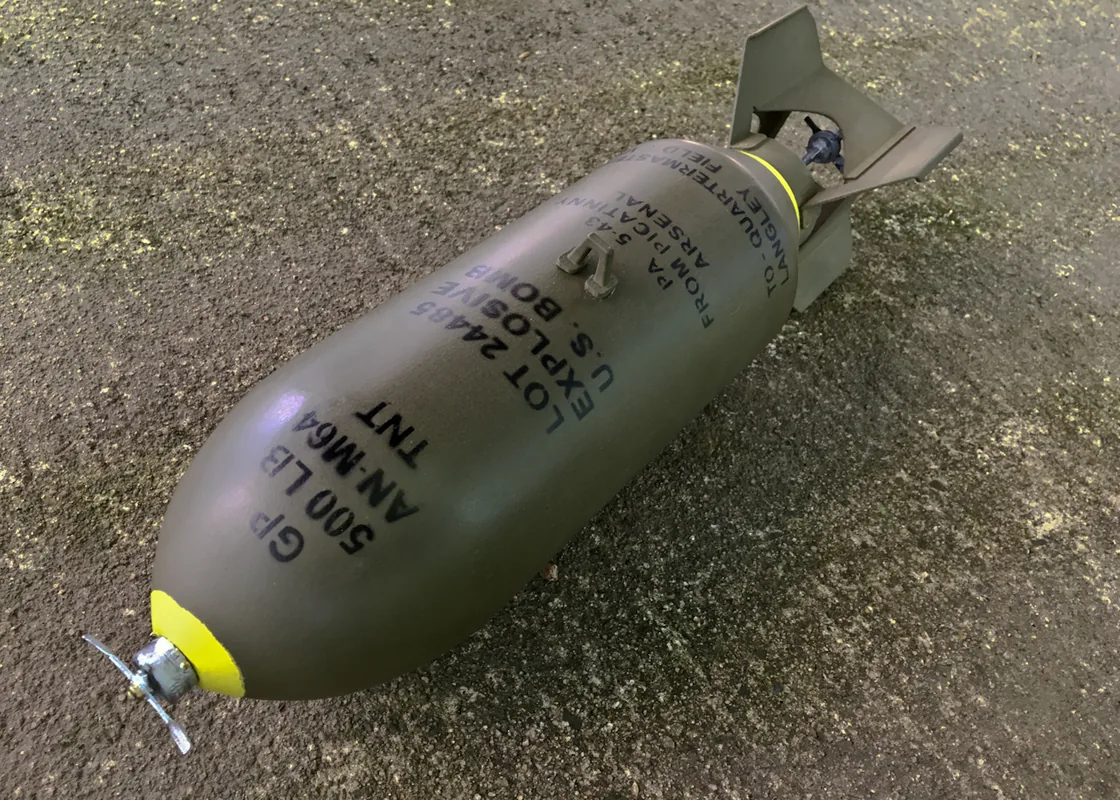 Field photo of a US AN-M64 500-pound general-purpose bomb on pavement, stencils legible